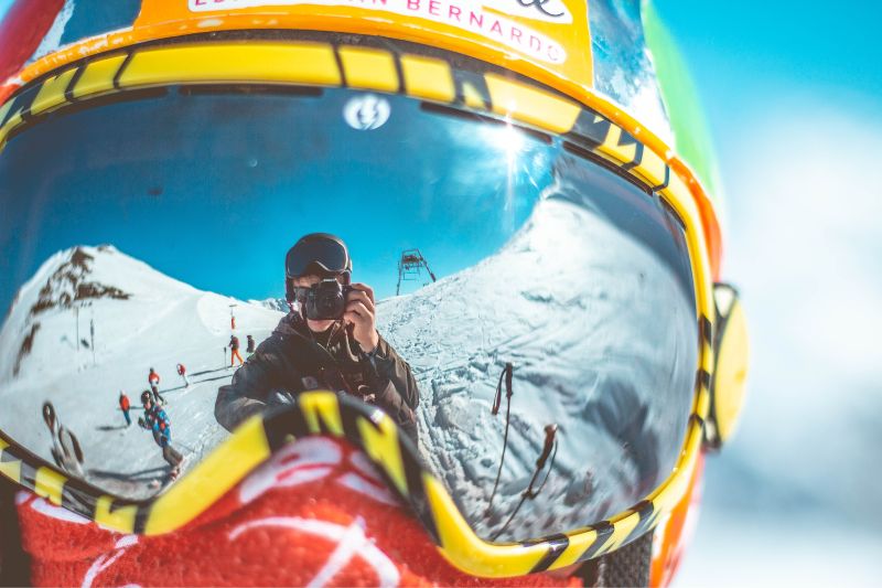 Reflective ski goggles with a skiier holding up a camera to the reflection 