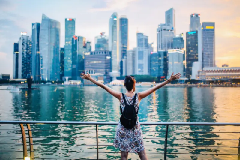 A lady wearing a dress stands infront of the Singapore skyline with her arms spread