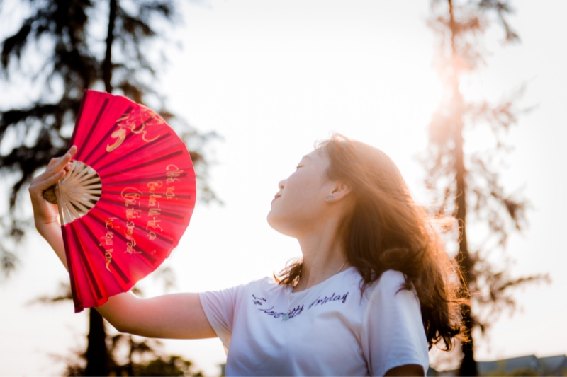 A lady holding a paper fan to cool down